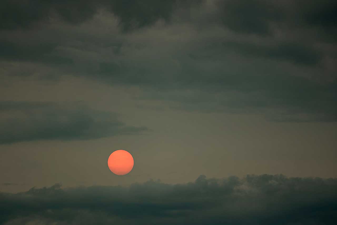 rote sonne vor dunklem wolkenhimmel in der dämmerung