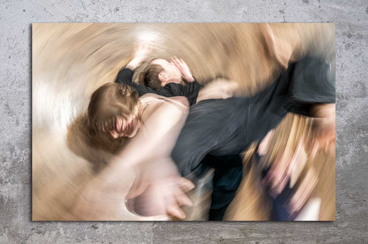 Dynamisches Foto von tanzenden Figuren in wirbelnder Bewegung auf grauem Betonboden, symbolisiert Liebe als Anker im Sturm der Versprechen